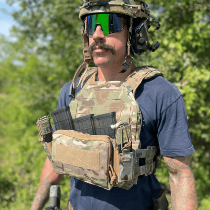 Person wearing tactical gear with a camouflage vest and helmet in an outdoor setting