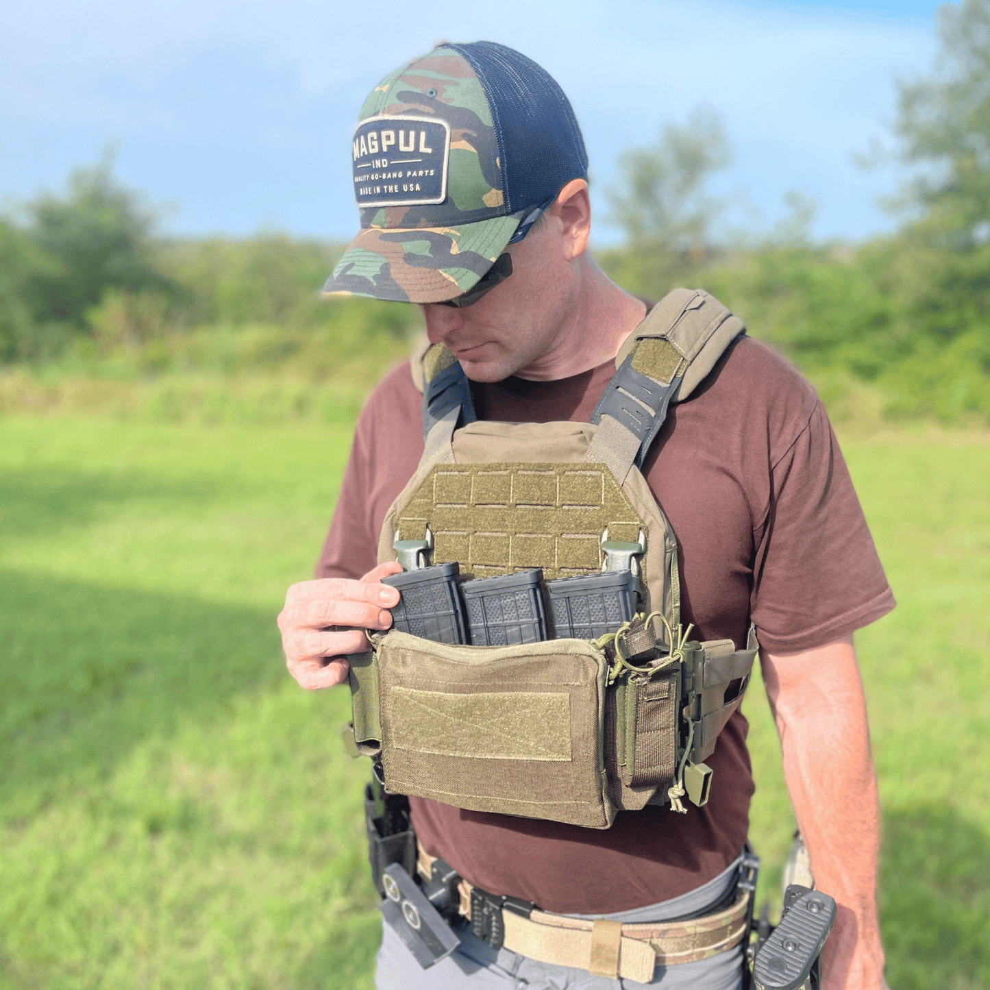 Man wearing a tactical vest and cap with 'Magpul' hat in an outdoor setting.