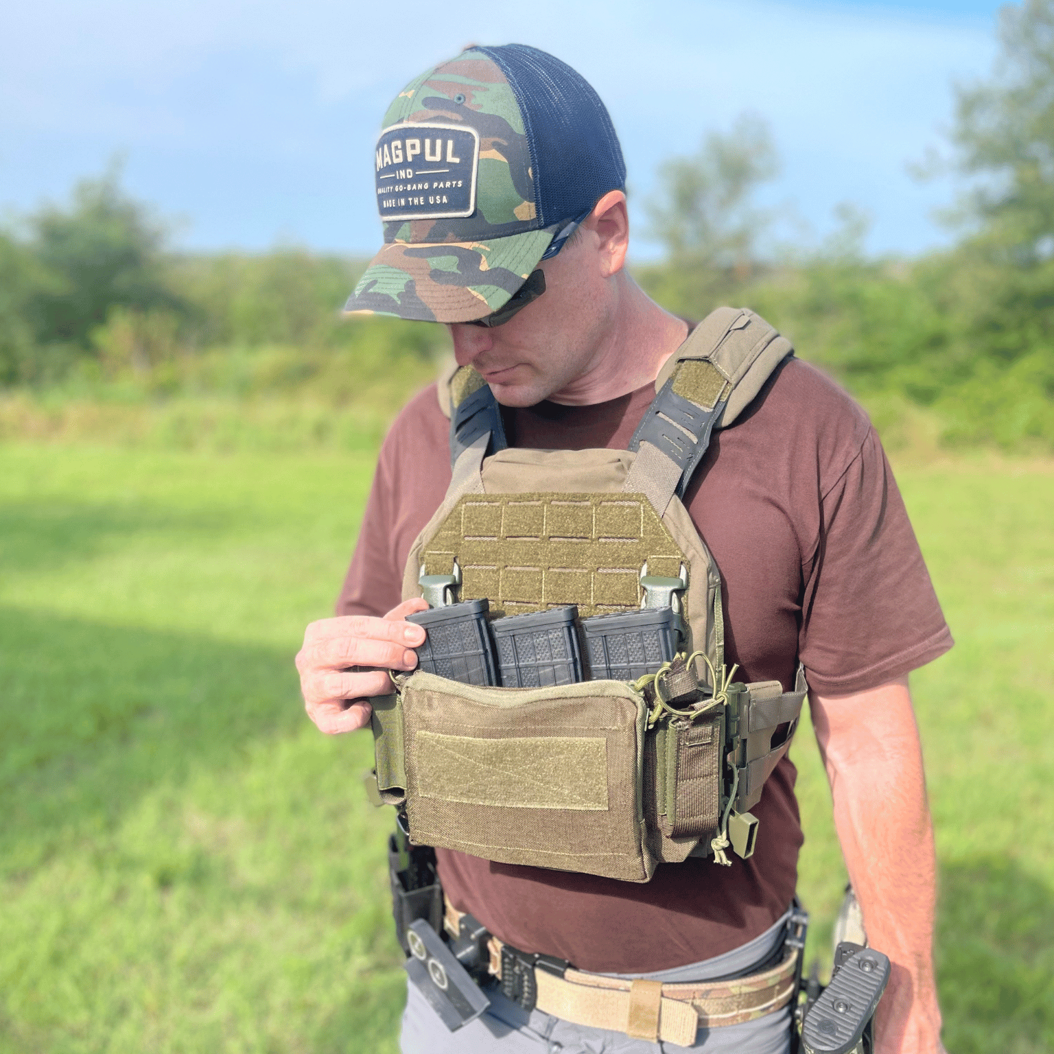 Man wearing a tactical vest and cap with 'Magpul' hat in an outdoor setting.