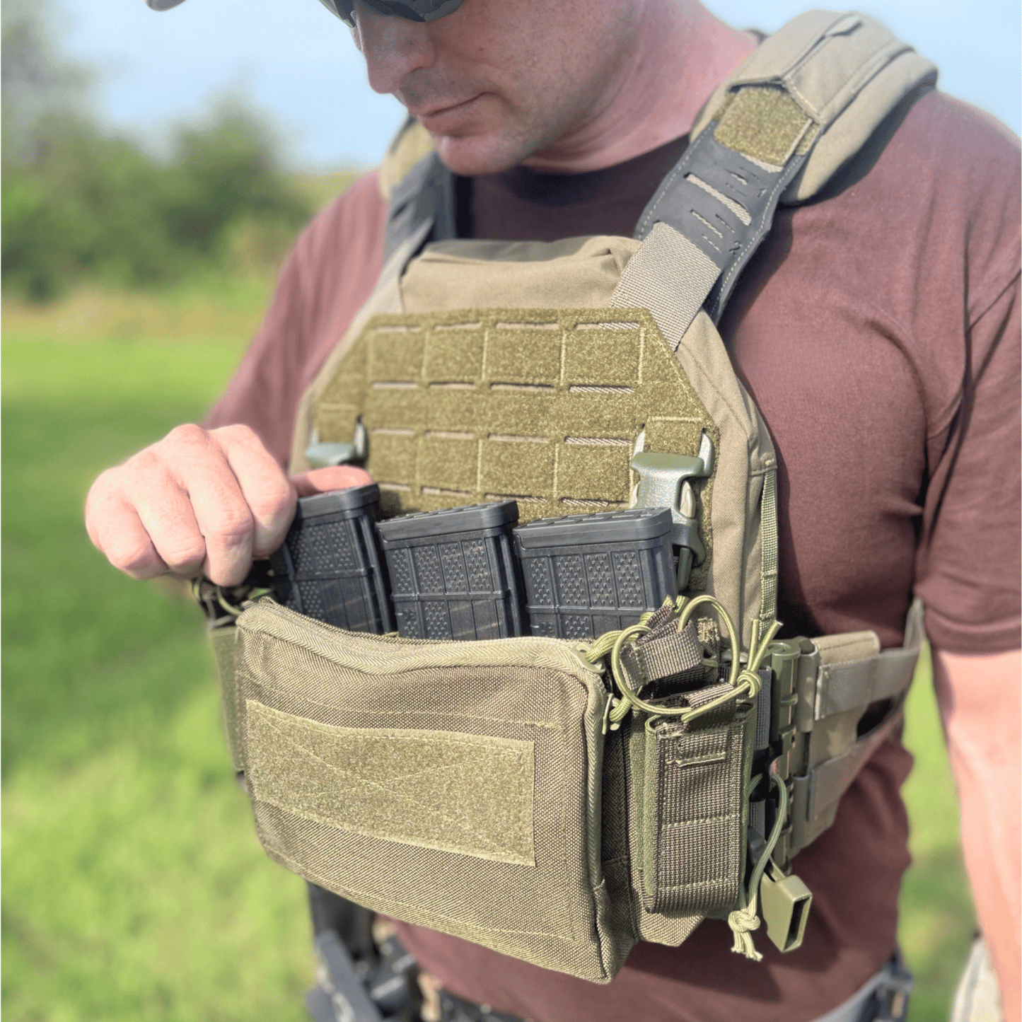 Person wearing a tactical vest with multiple pouches and magazines outdoors.