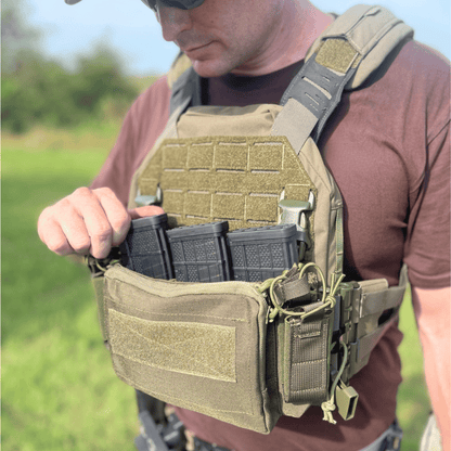 Person wearing a tactical vest with multiple pouches and magazines outdoors.