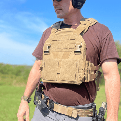 Man wearing a tactical vest in coyote brown against blue sky.